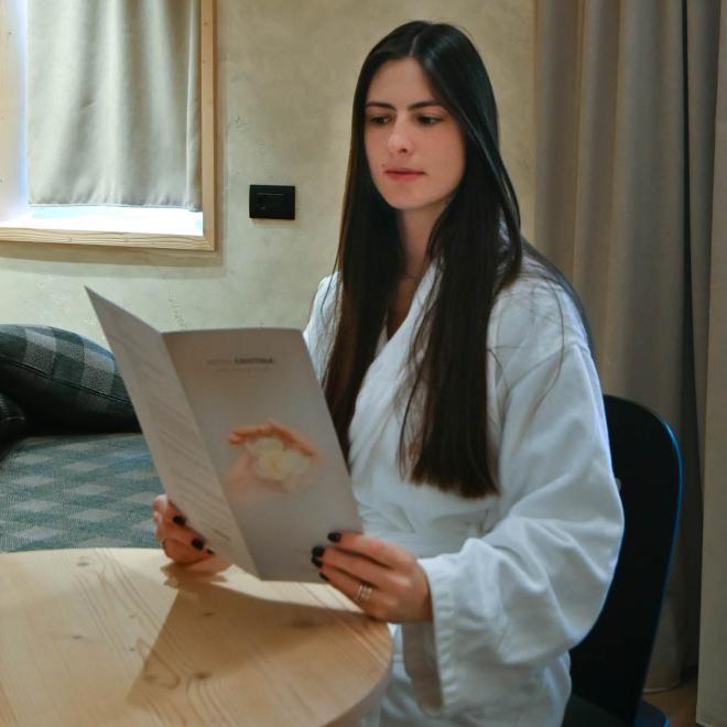Frau im Bademantel liest in einem gemütlichen Holzraum.